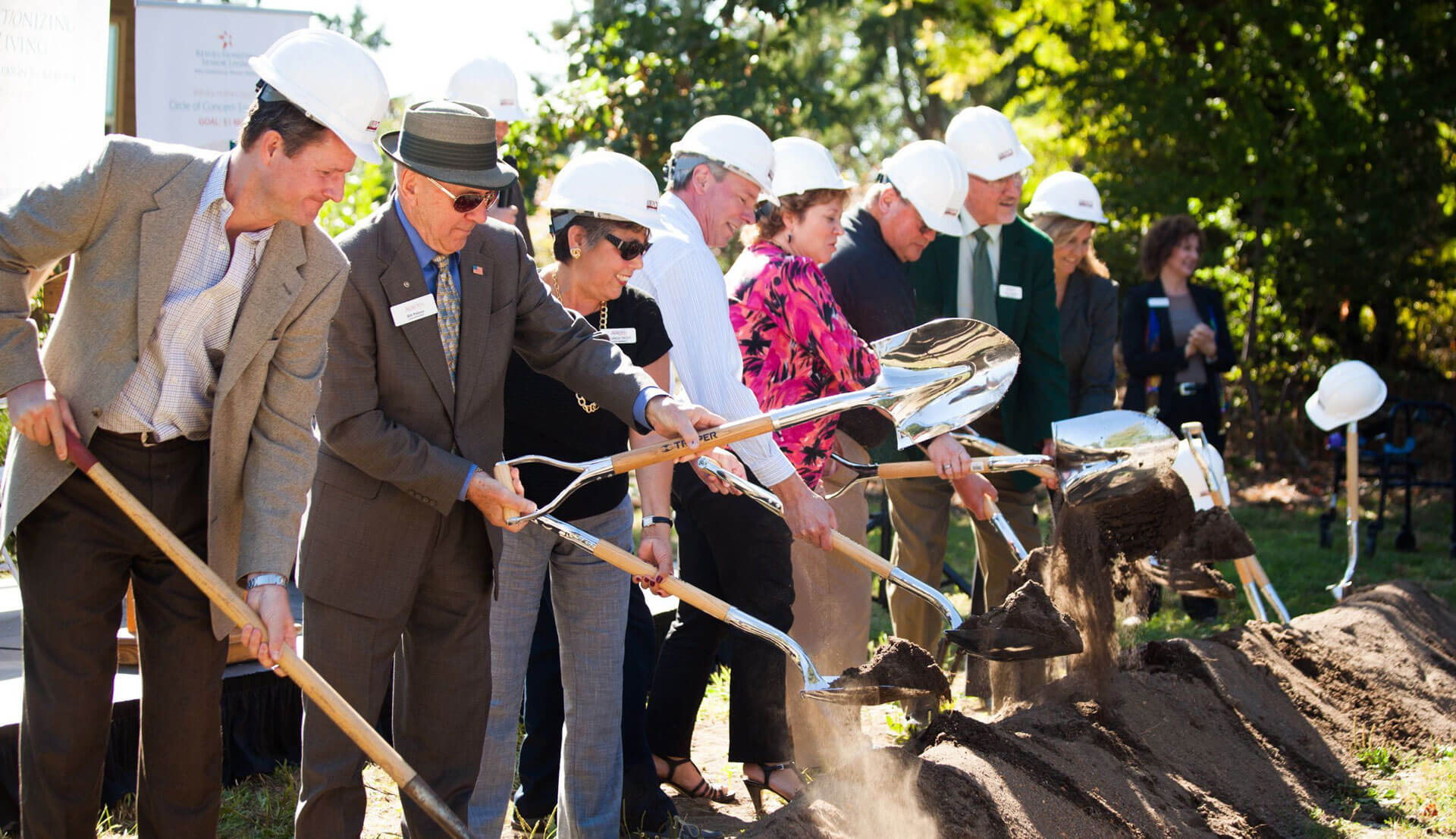 People in business attire and hard hats breaking ground with shovels