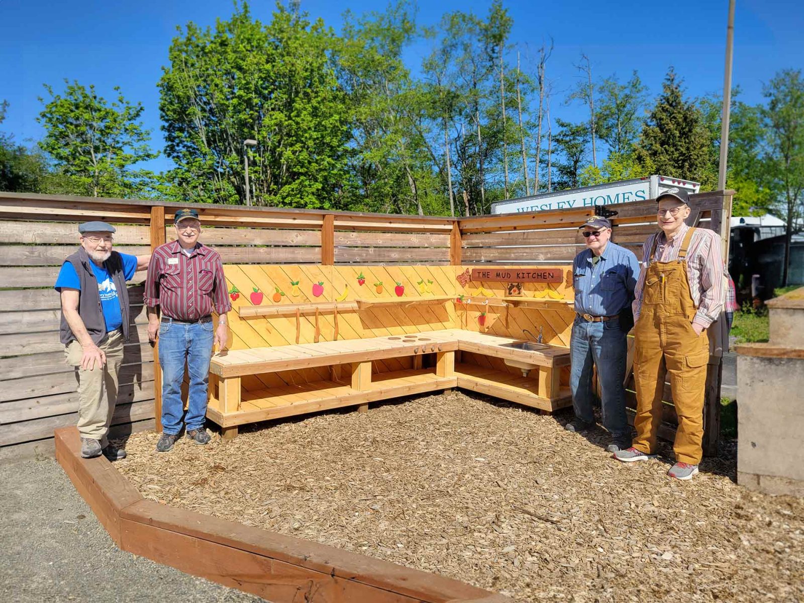 residents standing next to the wood play-kitchen they built