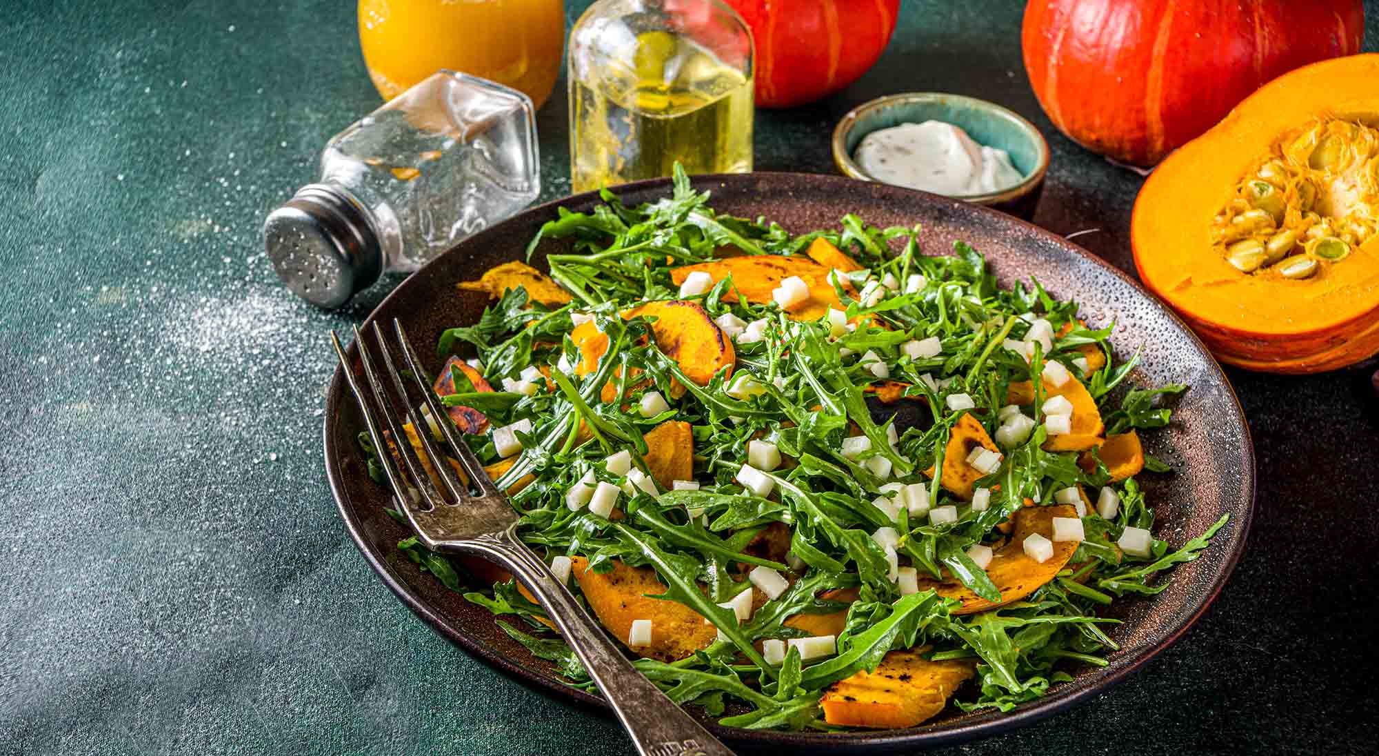 Homemade pumpkin salad with grilled pumpkin slices, arugula and cheese. Autumn pumpkin salad recipe, dark background copy space